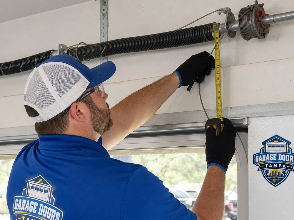 Technician measuring a torsion spring and inspecting the lift cable and cable drum